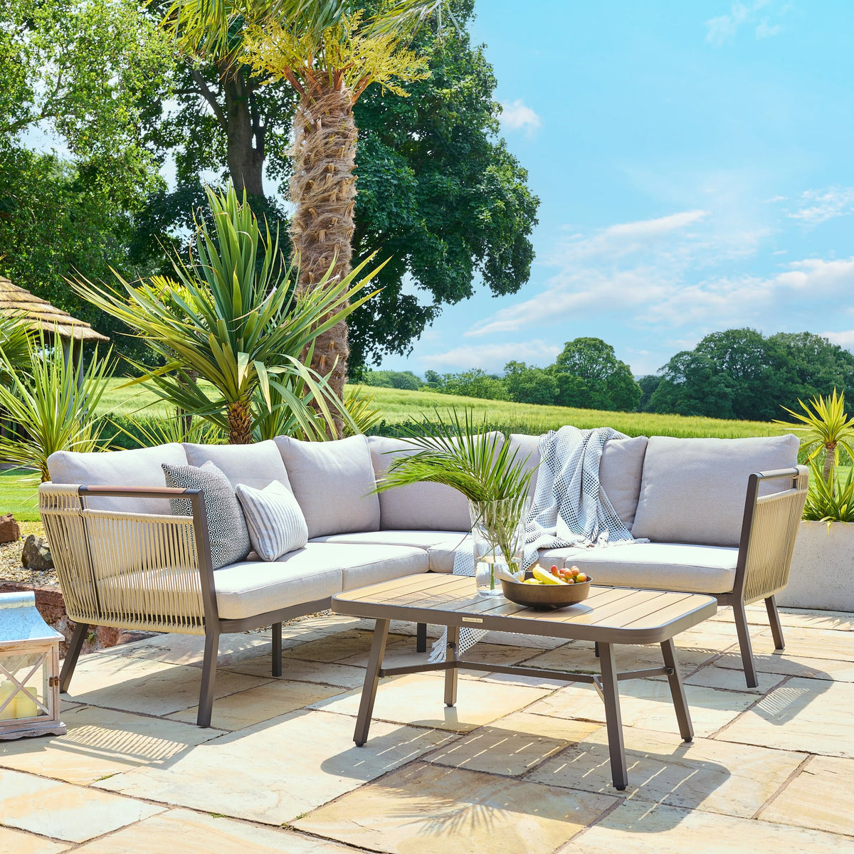 Bali corner sofa set in brown synthetic rattan with cream cushions and matching glass-top coffee table on patio
