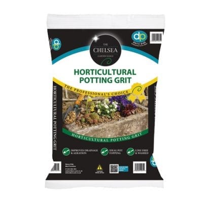 Gardener potting young plant into terracotta pot on potting bench with trowel and bag of multi-purpose potting compost